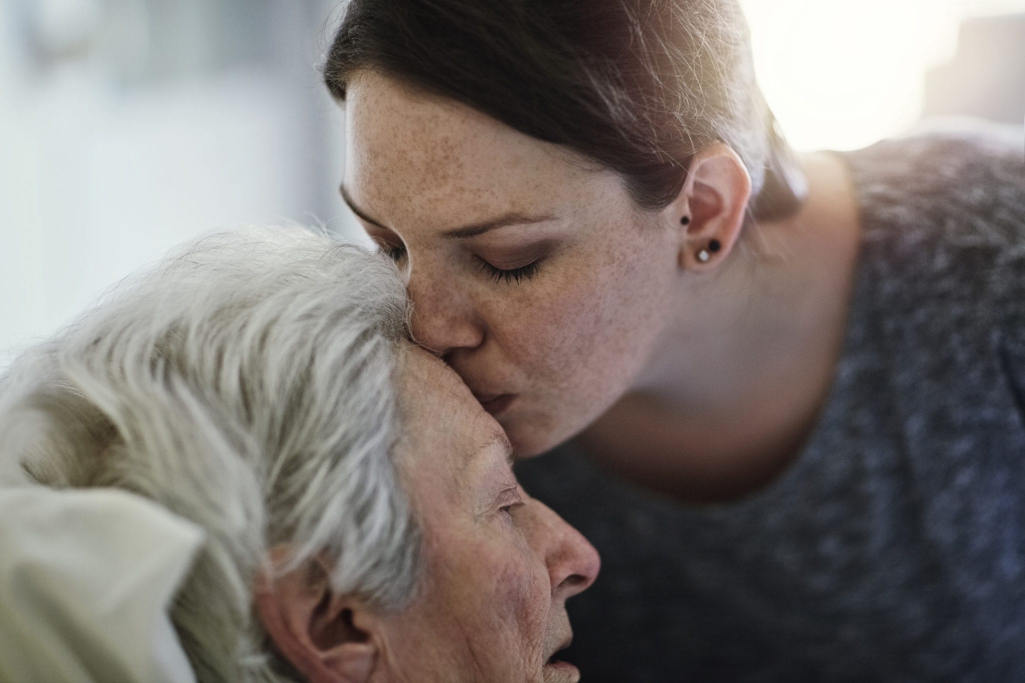 Caregiver adult daughter kisses mother who is in hospice care